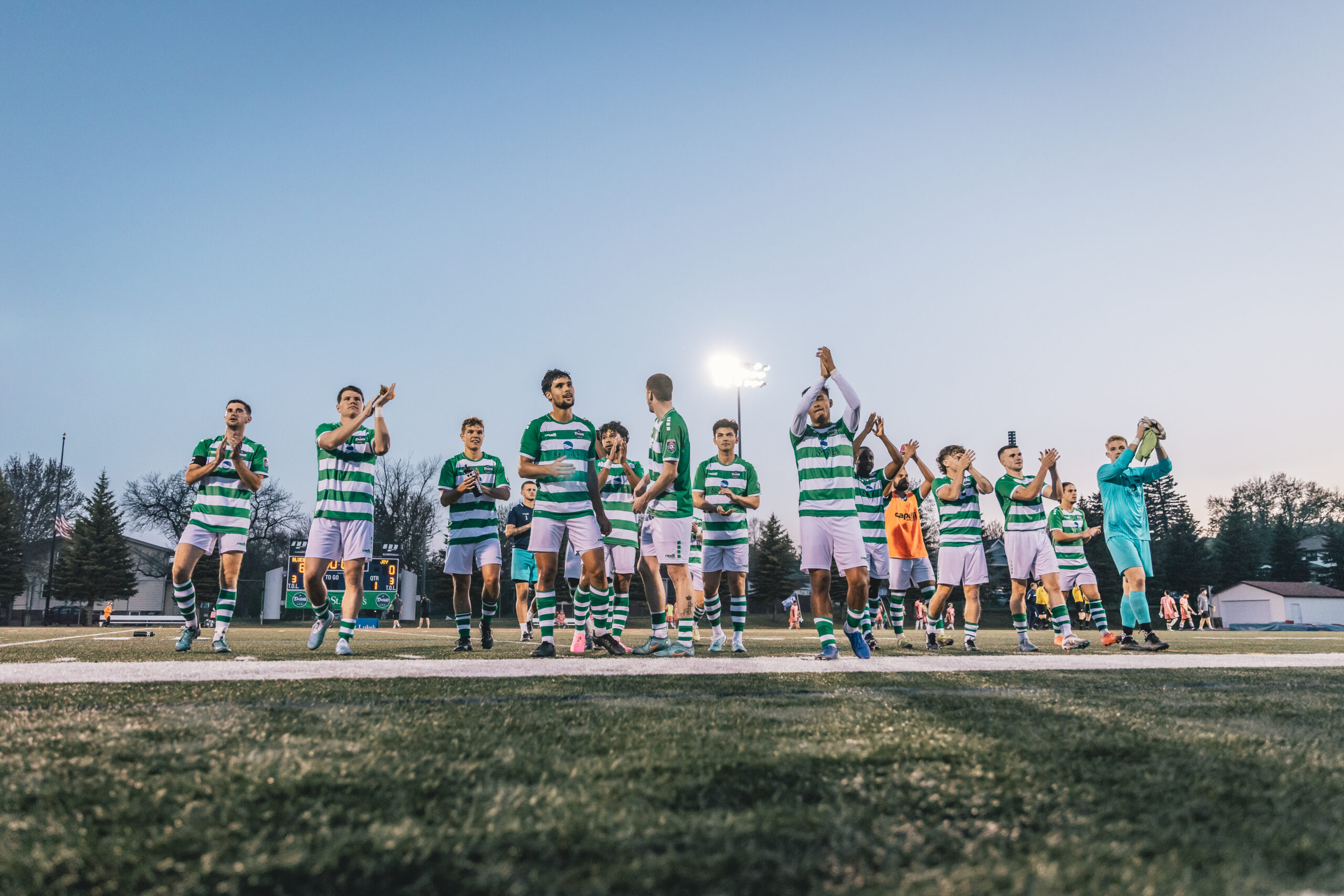 Soccer players in green and white hooped jerseys and white shorts celebrate
