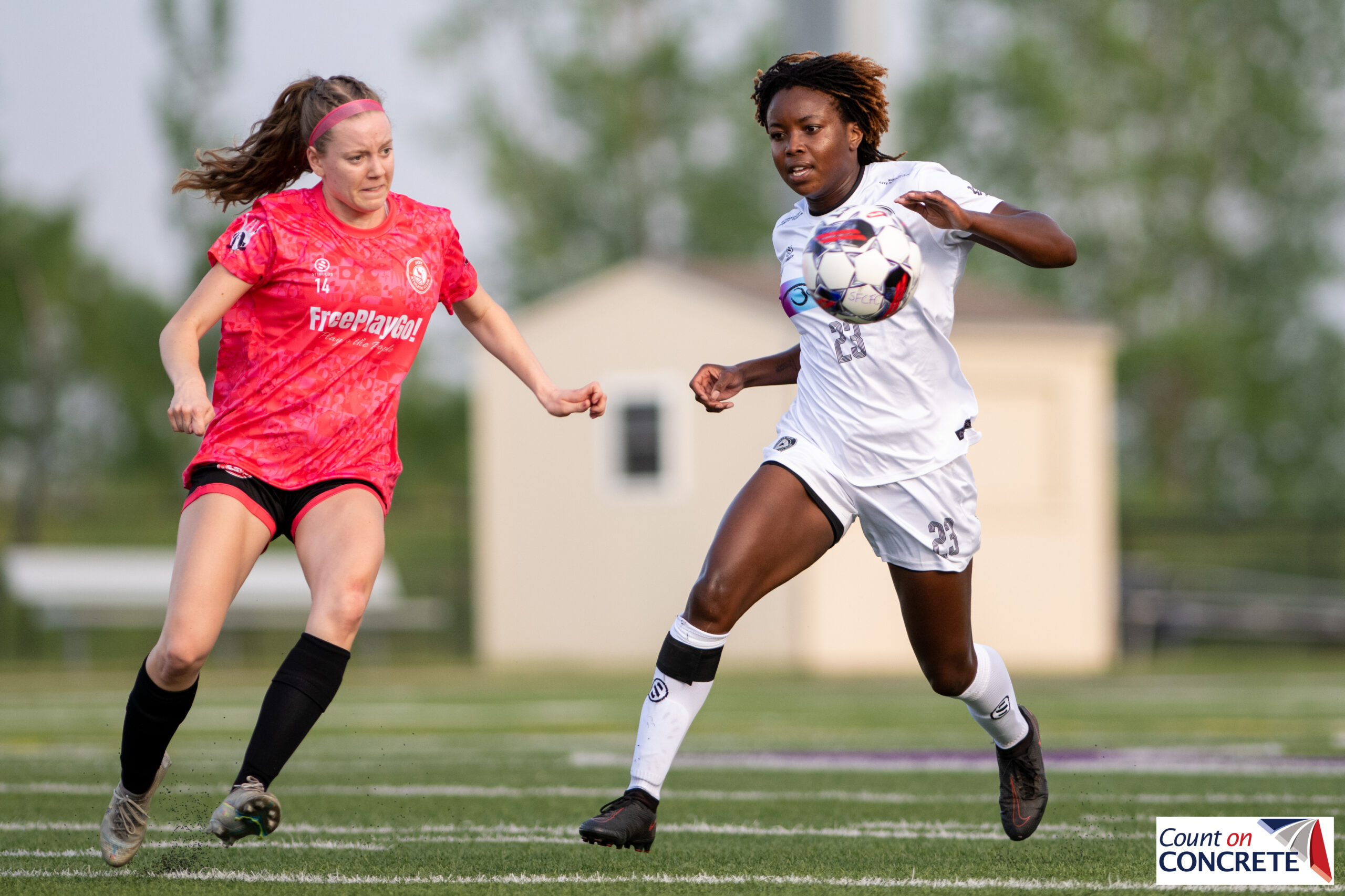 One woman in a hot pink jersey and another in an all white jersey compete for a soccer ball