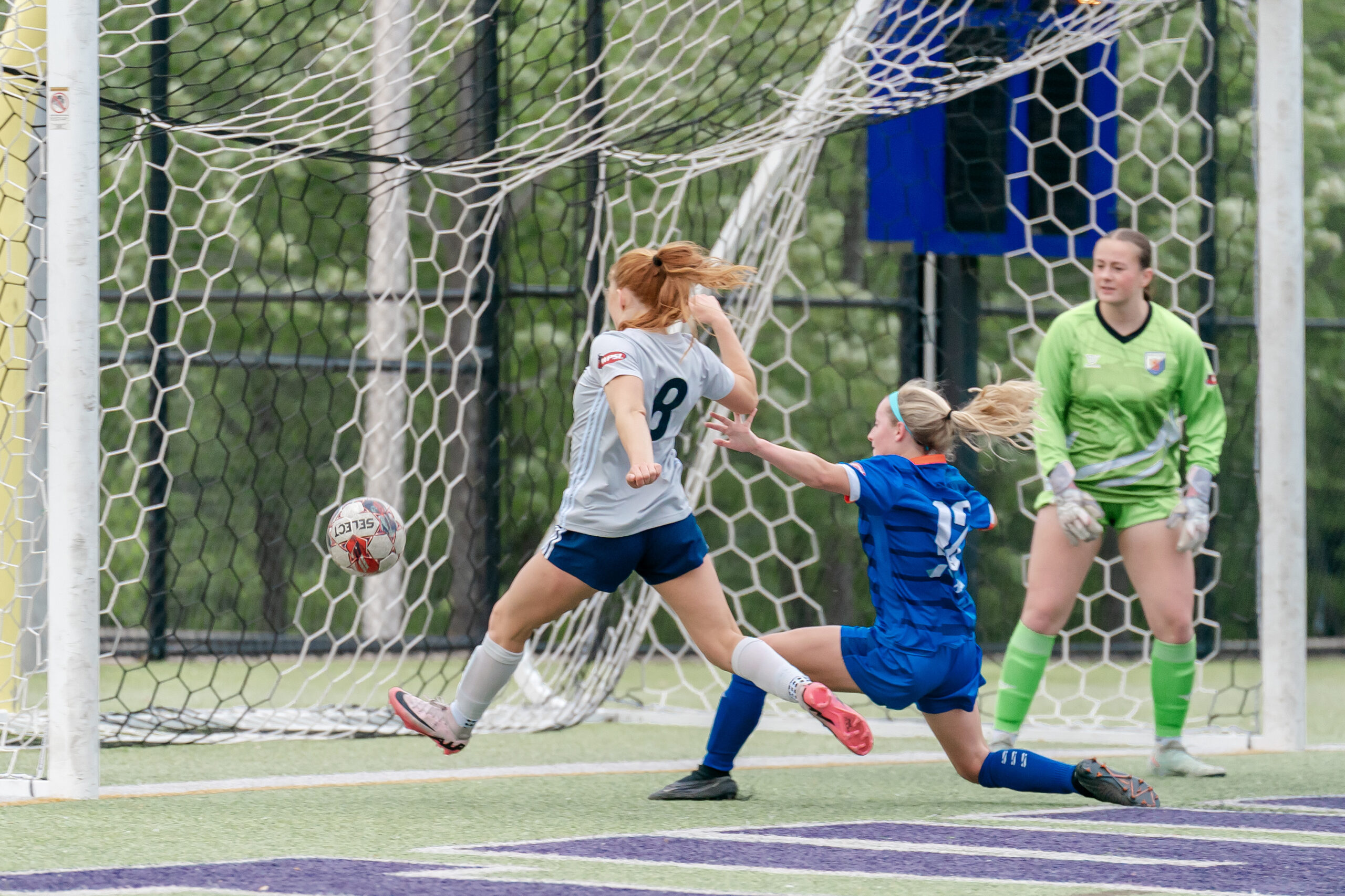 Red headed woman in grey jersey beats a blue-kitted defender to a ball