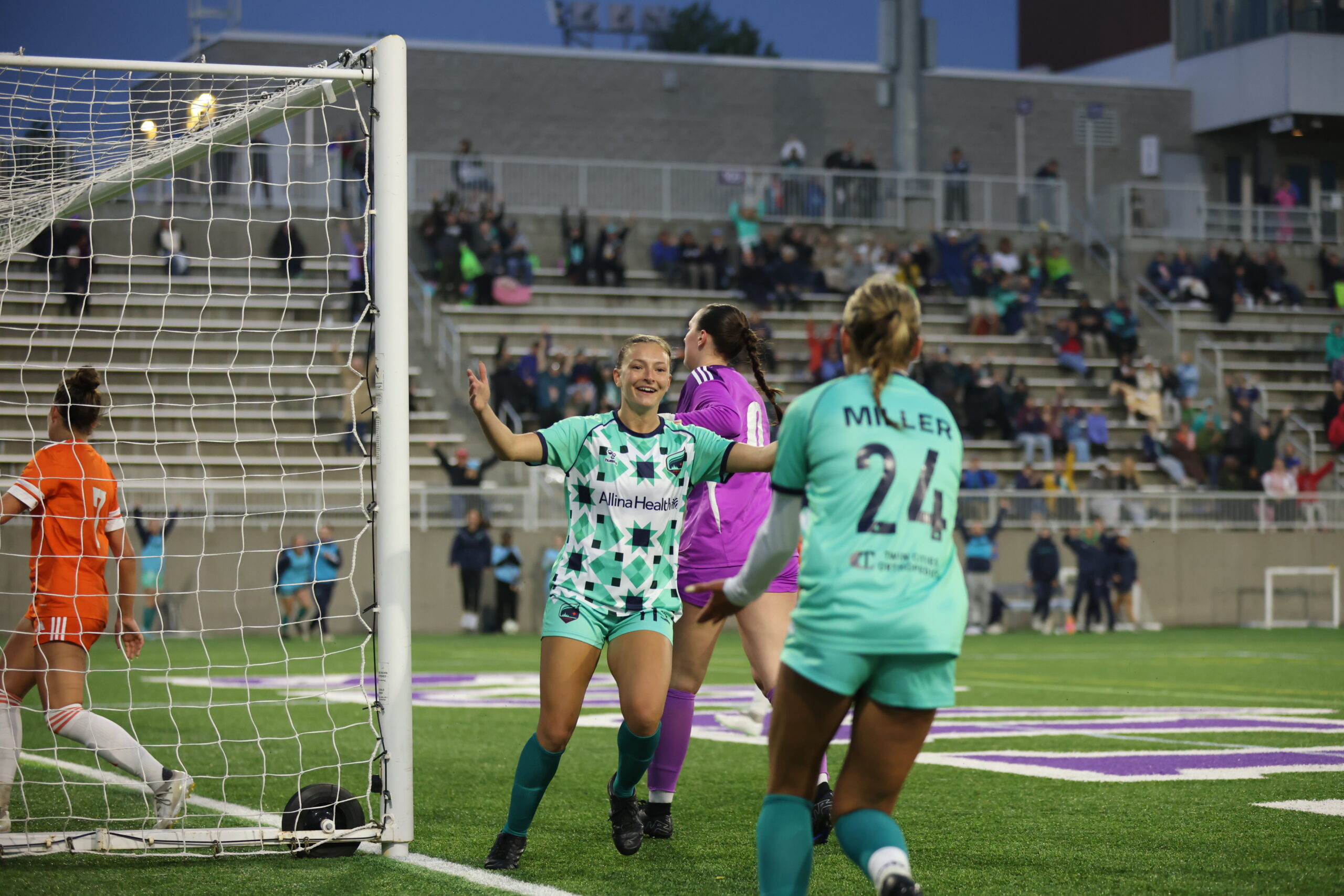 Two players in teal kits celebrate an Aurora FC goal