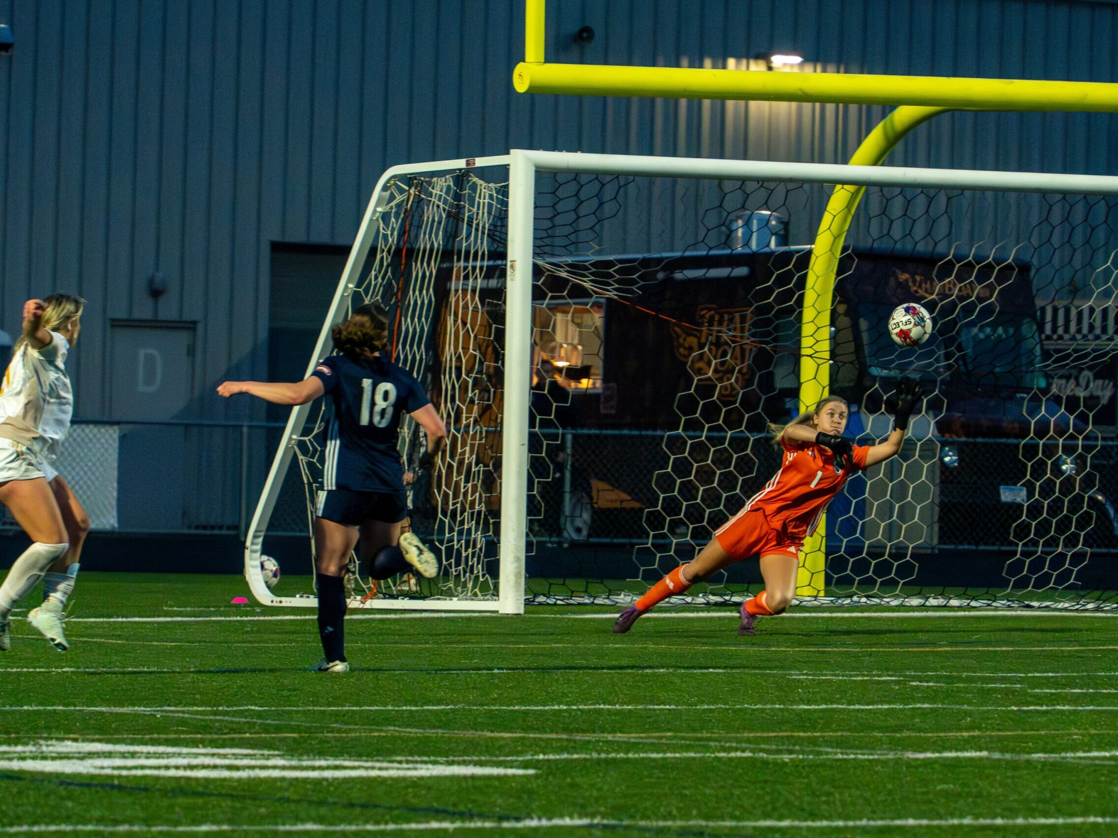 White shirted striker scores past a keeper in orange